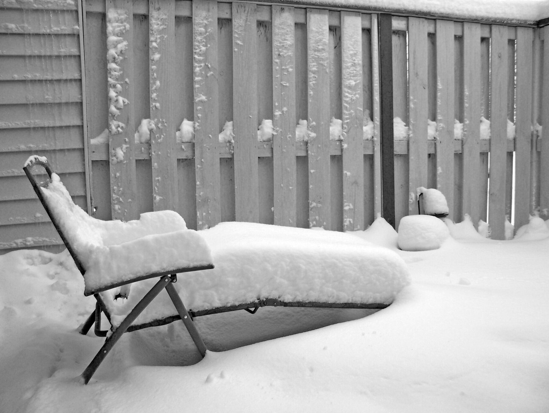 Snow-covered patio with a lawn chair illustrating winter-ready patio design using concrete and gravel for Iowa homeowners.