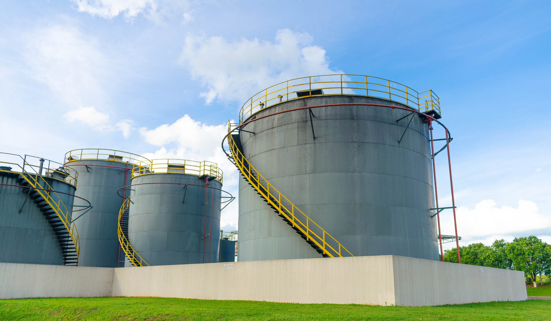 Industrial bulk material storage tanks on concrete pads with yellow staircases used for fuel material storage at a processing facility.